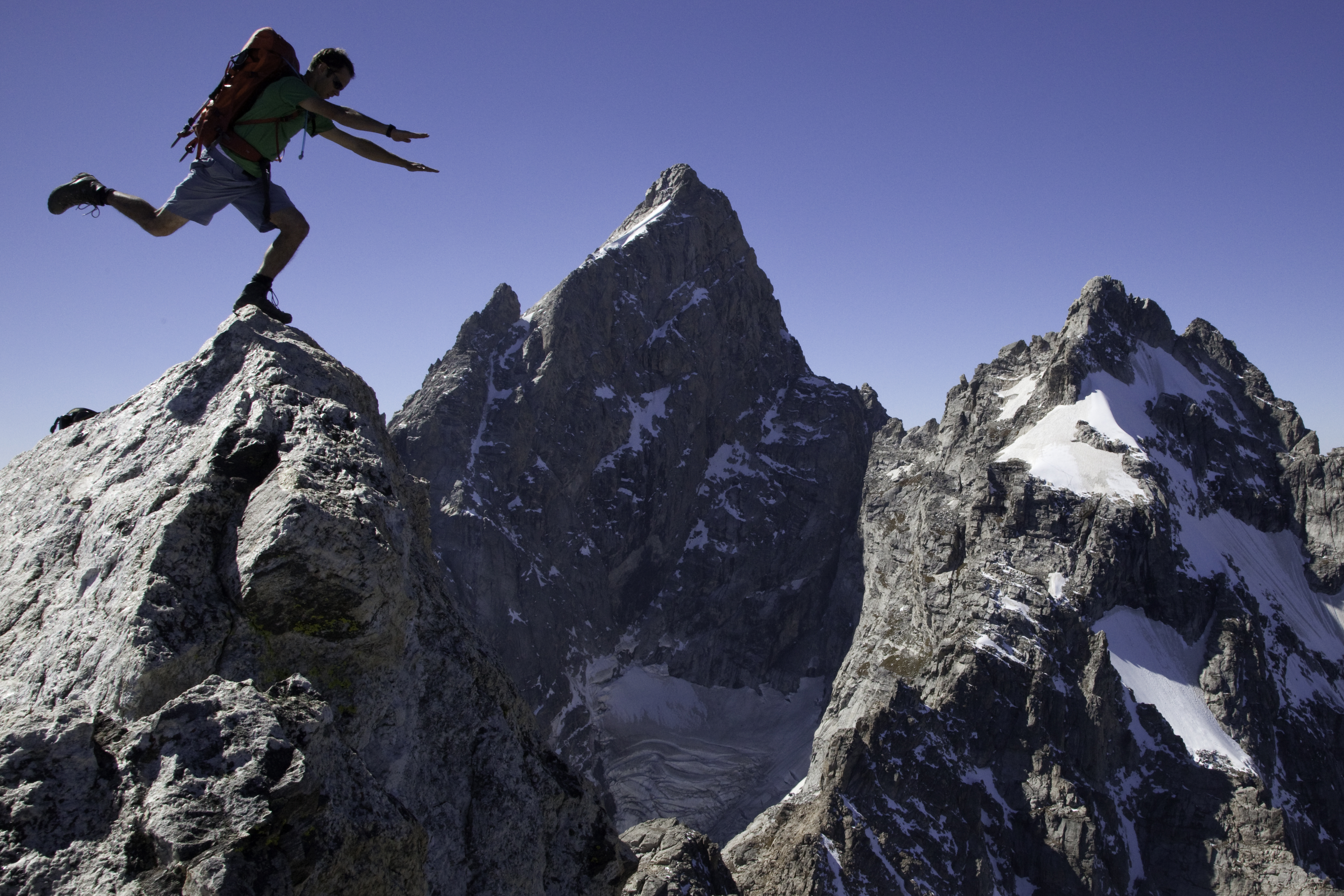 Climber showing off on the summit of Teewinot in Grand Teton National Park. Climber on the summit of Teewinot with the Grand Teton and Mount Winster in the background.