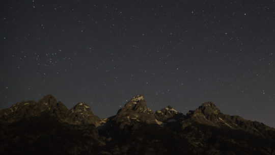 Stars and Constellations Appear In The Night Sky Above The Grand Teton Range